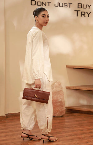 Side view of an off-white tunic set with cuffed-hem trousers, styled with a brown leather handbag.