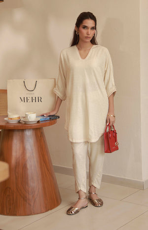 Model wearing an off-white embroidered silk tunic with matching trousers and metallic flat sandals.