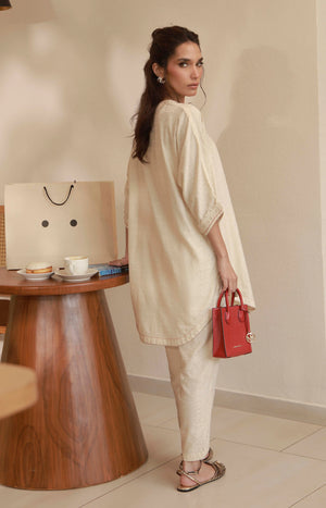 Back profile of a model in an off-white long tunic set paired with a small red handbag.