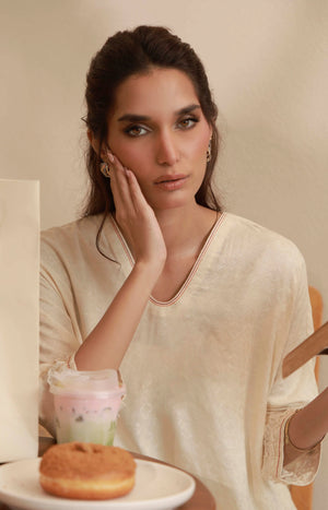 Portrait shot highlighting the fine embroidery on the neck and cuffs of an off-white silk tunic.