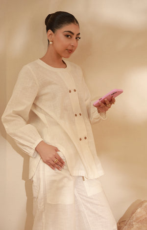 Medium close-up showing the detail of an off-white buttoned tunic top and cuff-hem trousers.
