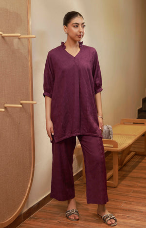 Front view of a plum purple matching set with a ruffle V-neck tunic and matching wide-leg trousers.
