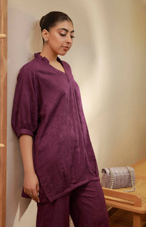 Close-up of the plum purple V-neck tunic showing the ruffled neckline texture and sleeve detail.
