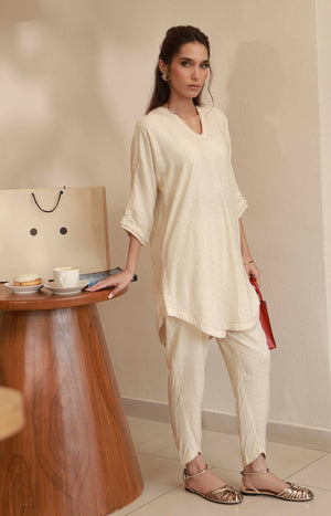 Side pose showing a loose-fit off-white embroidered kurta set with matching tapered pants.
