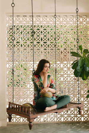 Woman sitting on a wooden swing in a decorative indoor setting with plants and lattice wall.

